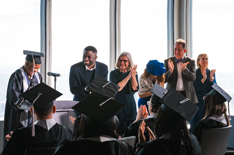 Graduation ceremony with graduates in caps and gowns clapping and celebrating.