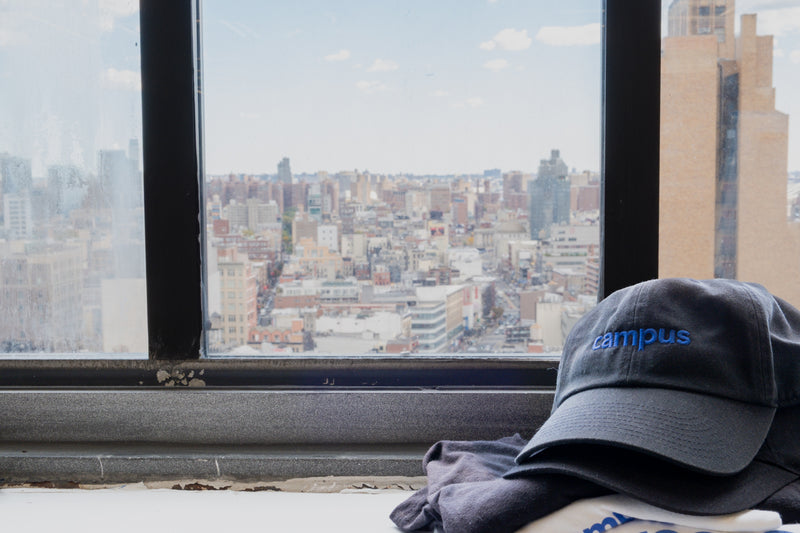 Cap and shirt on a ledge with a cityscape view from a high-rise window.